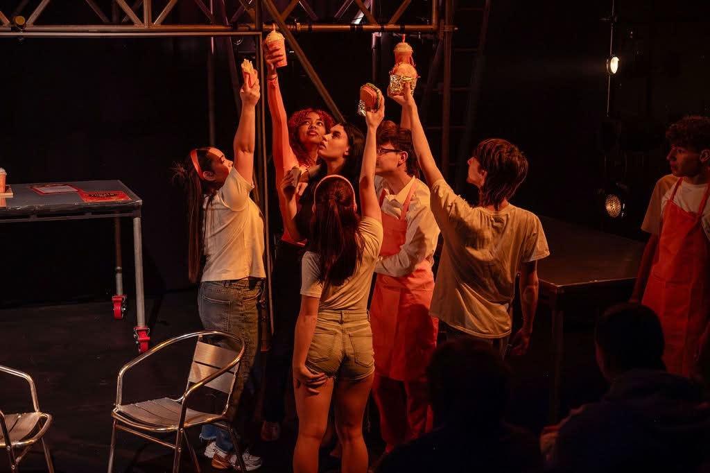 Cast gathered together onstage under warm theatre lighting